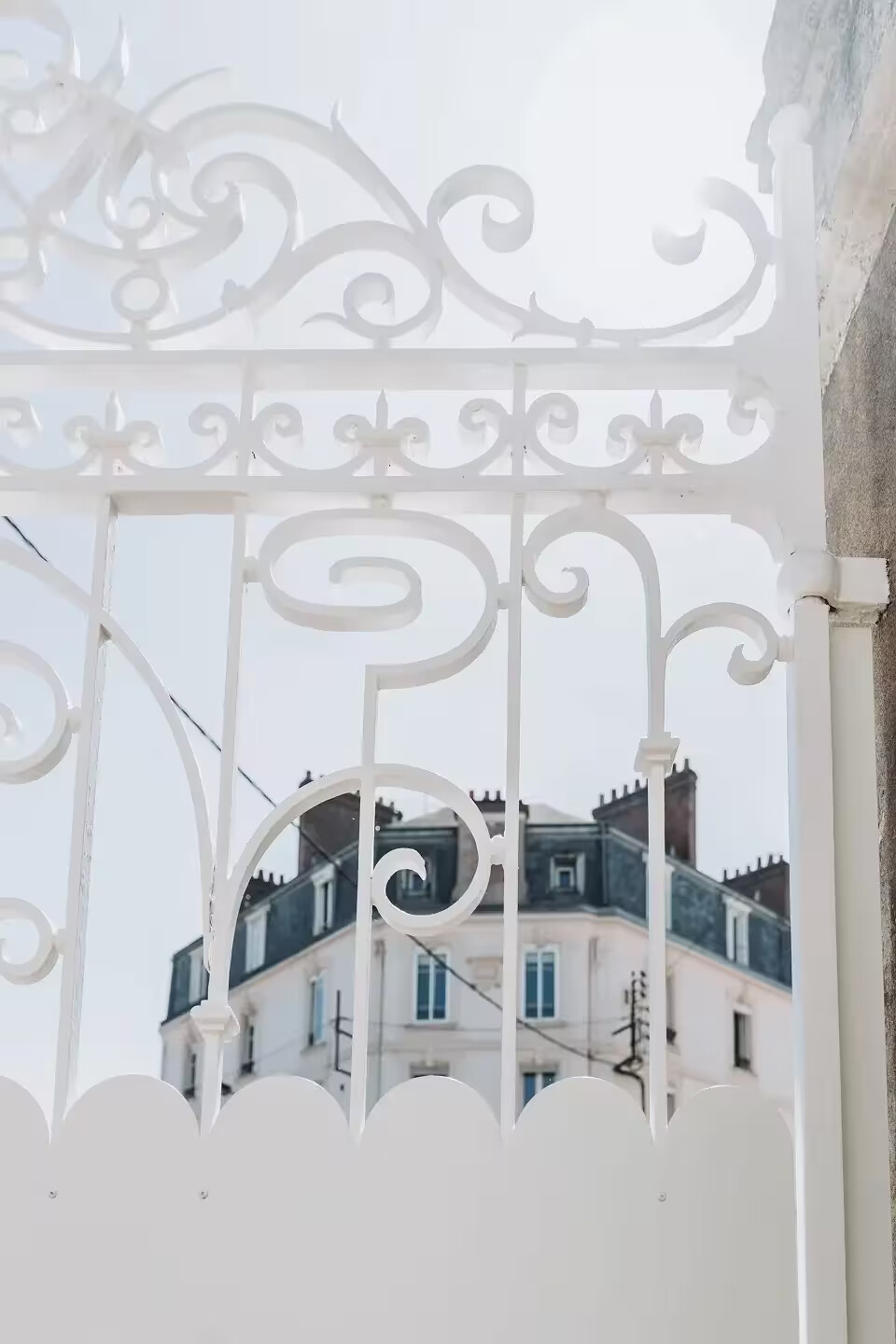 Détail des volutes en fer forgé restaurées et repeintes en blanc d'un portail rénové par Coyac à Nantes, avec tôle festonnée d'occultation en partie basse
