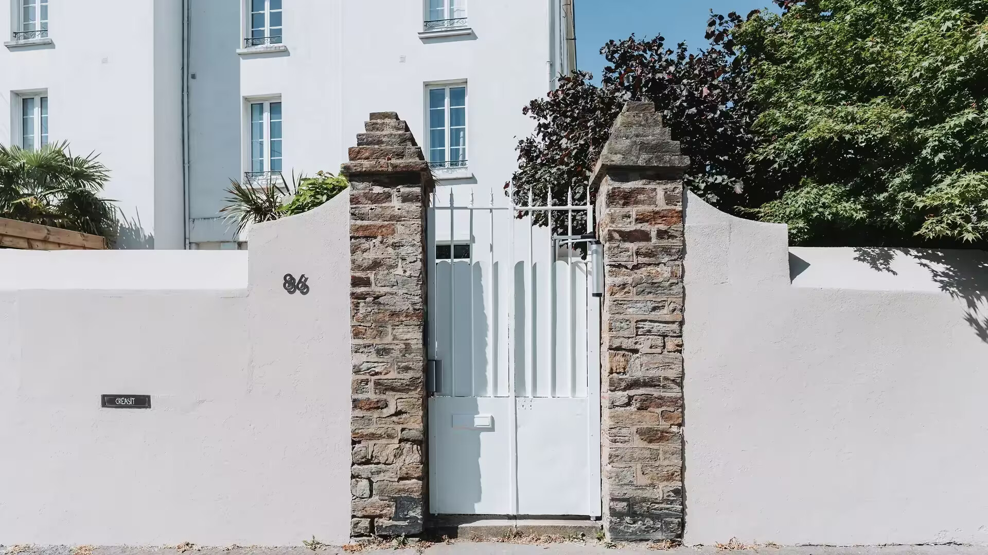 Portillon en fer forgé rénové et modernisé par Coyac à Nantes, repeint en blanc avec tôle festonnée et contrôle d'accès, intégré entre piliers en pierre