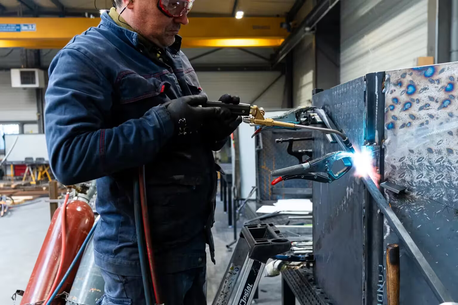 Compagnon métallier de Coyac soudant au chalumeau sur un ouvrage en cours d'assemblage dans l'atelier, étincelles et arc lumineux